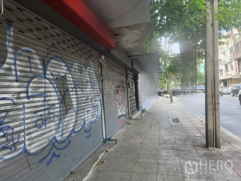 店屋 出租在Watthana, Bangkok - 主干道旁的人行道视角，成排店面卷闸门和行道树