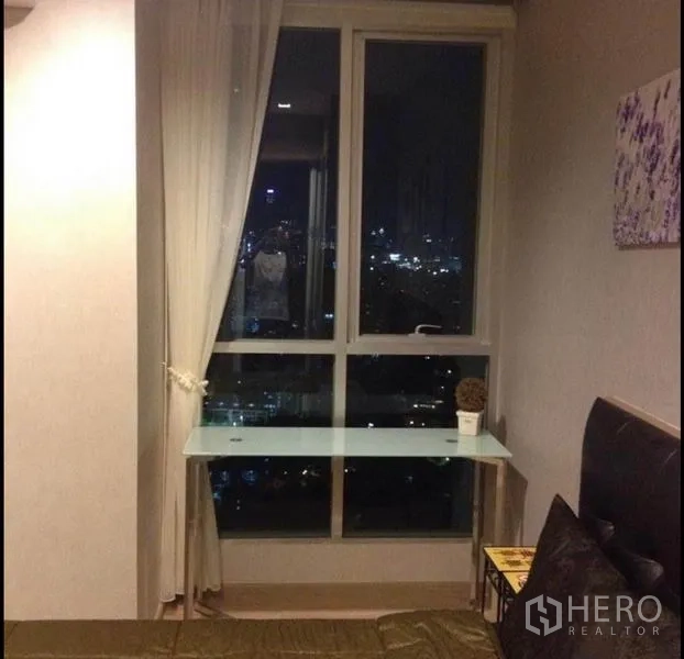 公寓 出售在Phaya Thai, Bangkok - 卧室一角，大窗与纱帘、玻璃书桌，夜色城市景观。