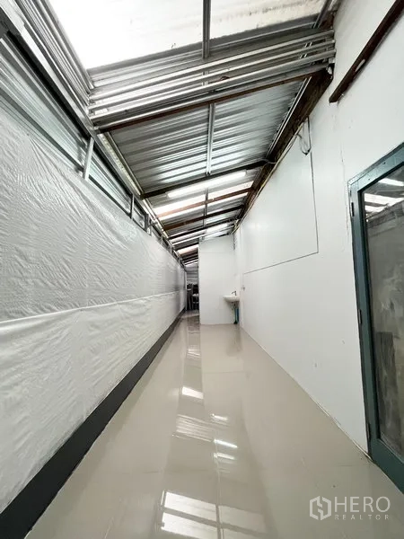 Warehouse for rent in Wang Thonglang, Bangkok - Corridor view with skylight panels and a wall-mounted sink at the far end.