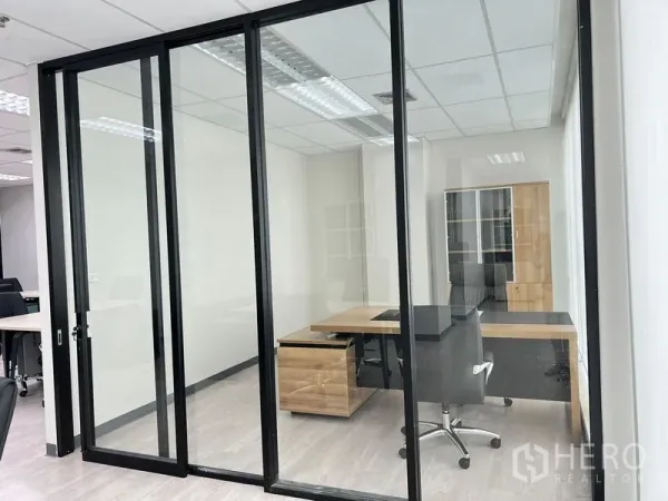 Office Space for rent in Sathon, Bangkok - Private executive office behind glass with an L-shaped wooden desk and storage cabinet.