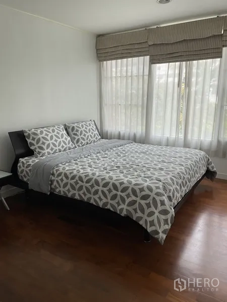 Condominium for rent in Pathum Wan, Bangkok - Second bedroom with king bed, patterned duvet, corner windows and timber flooring in a Bangkok condo.