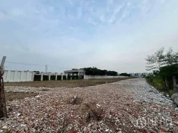 ที่ดิน ให้เช่าในLat Krabang, Bangkok - ที่ดินรูปสี่เหลี่ยมผืนผ้ายาวในลาดกระบัง ถมวัสดุหิน มีรั้วและต้นไม้ ใต้ท้องฟ้ามีเมฆ