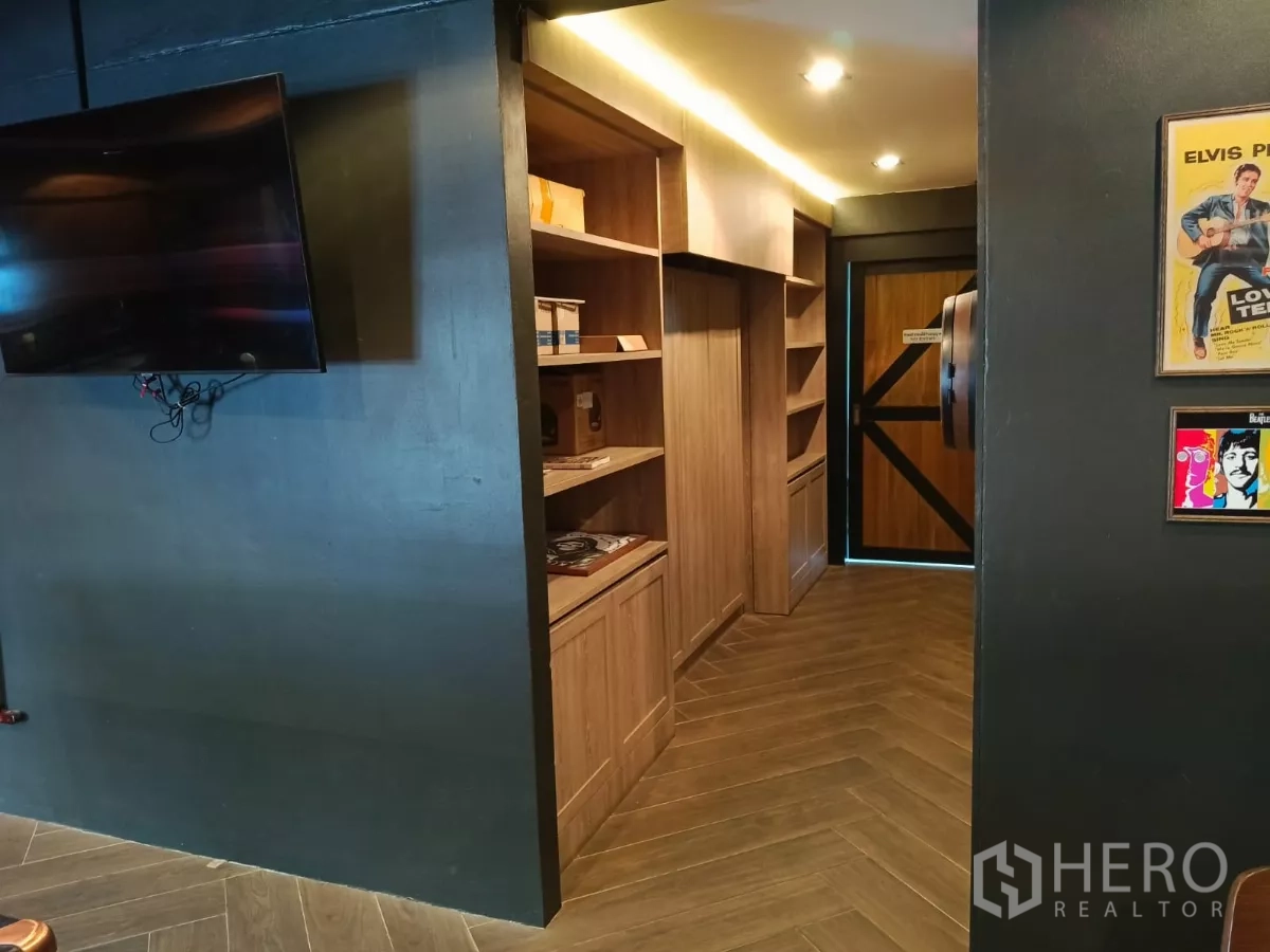 Retail Space for rent - Open lounge with wall‑mounted TV and corridor of wooden shelving to a barn‑style door.