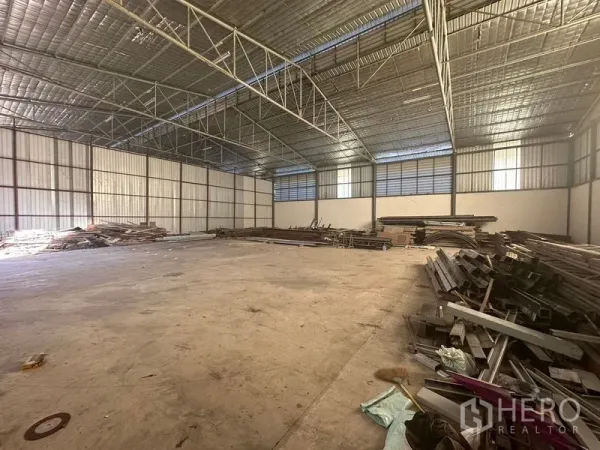 Warehouse for rent in Saphan Sung, Bangkok - Open warehouse hall with clear-span ceiling, natural light windows and metal beams stored along the sides.