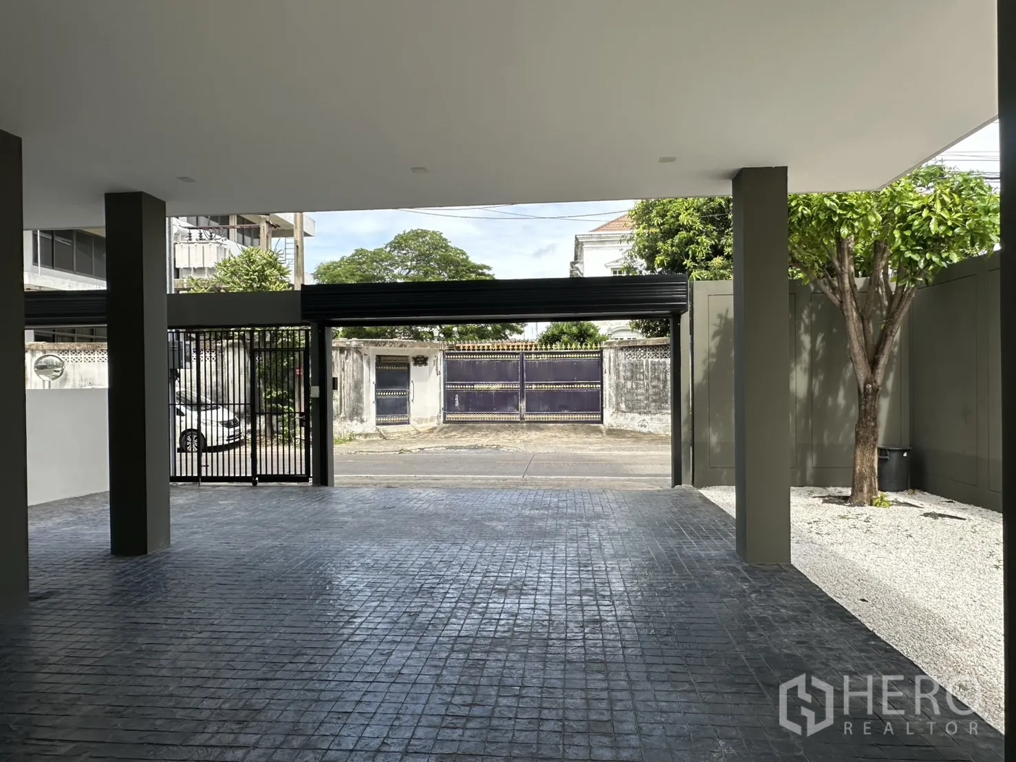 Home Office for rent or sale in Suan Luang, Bangkok - Wide carport facing the street with sliding metal gate and shaded tree.