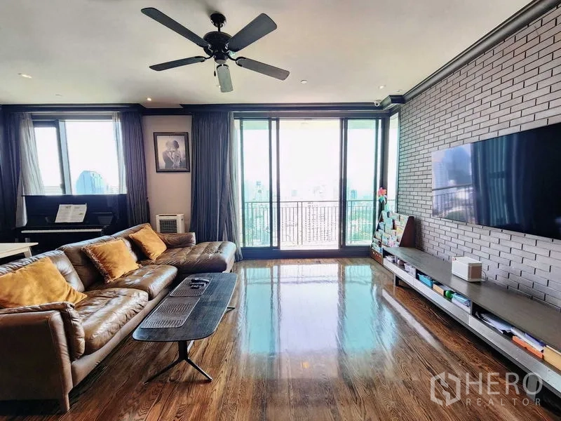 Condominium for sale in Khlong Toei, Bangkok - Living room facing TV and sliding doors to balcony with skyline backdrop.