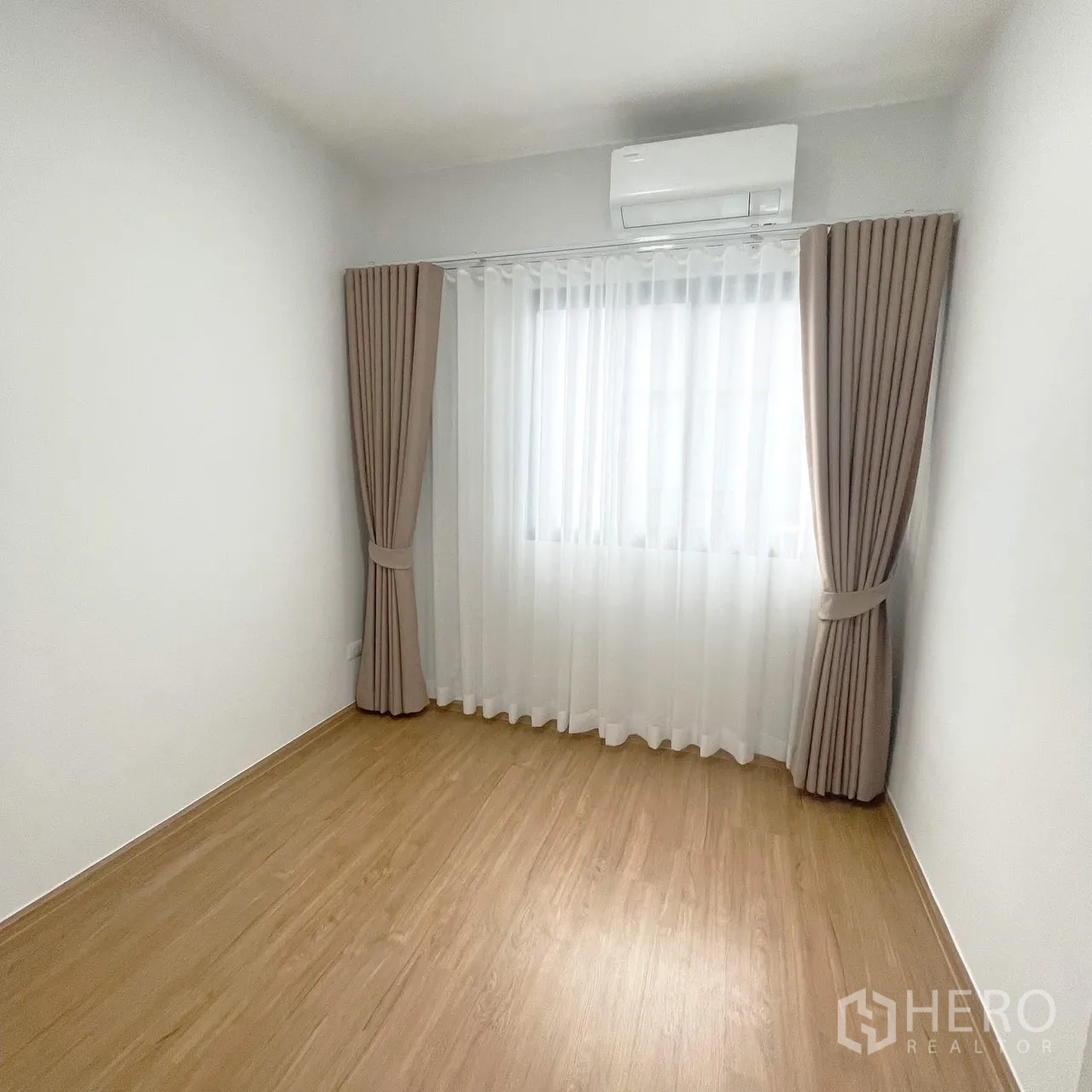 Townhouse for rent in Bang Phli, Samut Prakan - Empty bedroom with wood-look flooring, double curtains, and a wall-mounted air conditioner.