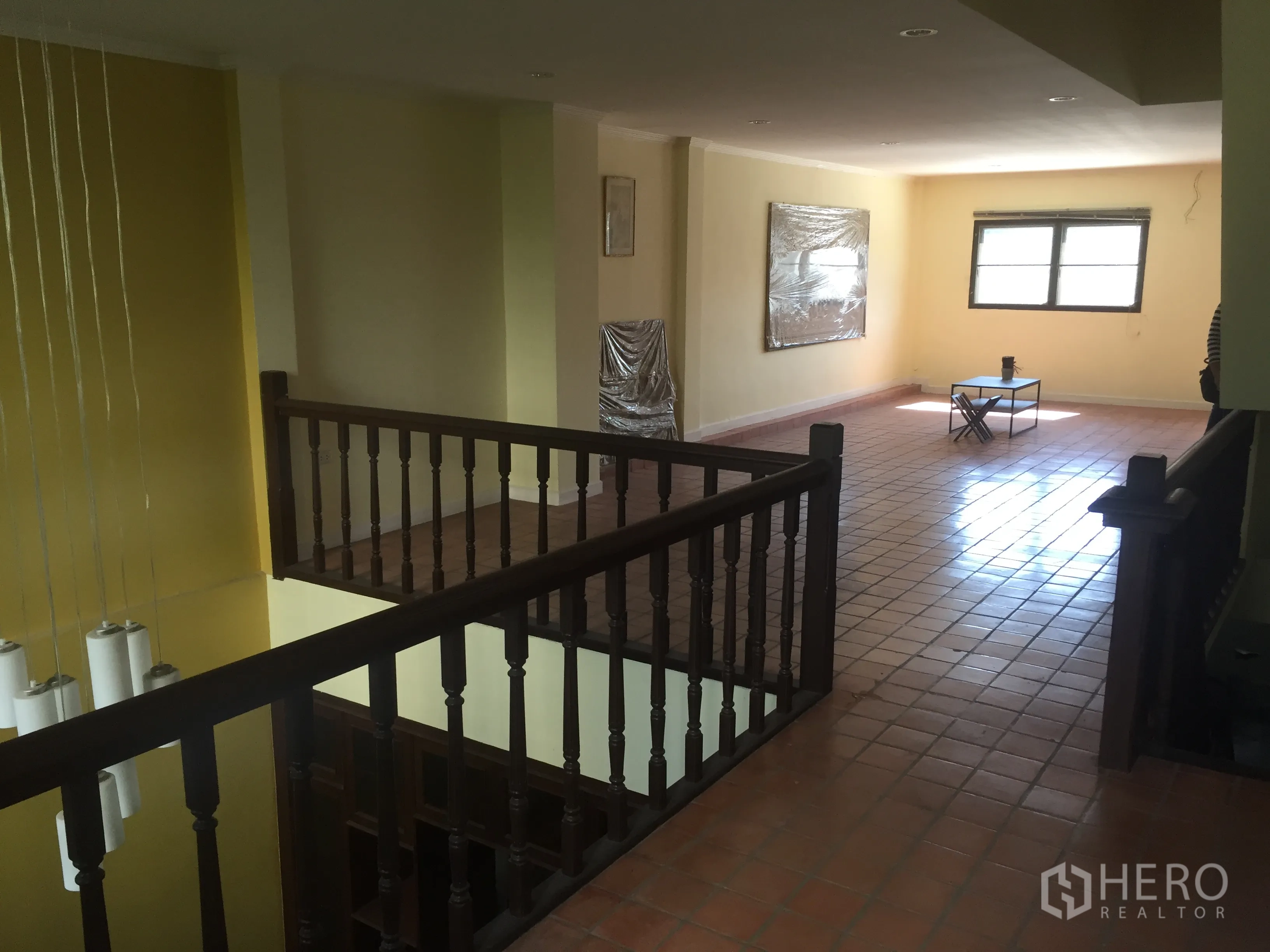 Townhouse for rent in Khlong Toei, Bangkok - Upper landing with wooden balustrade overlooking a double-height void and bright lounge area.