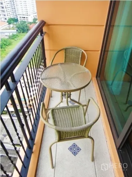 Condominium for rent in Khlong Toei, Bangkok - Narrow balcony with glass-top bistro table, two wicker chairs, and city view.