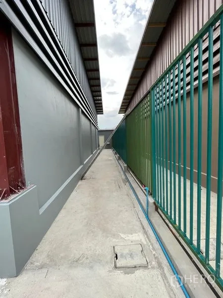 คลังสินค้า ให้เช่าในKhlong Sam Wa, Bangkok - ซอยบริการแคบระหว่างโกดังข้างเคียง มีรั้วสีเขียว ท่อประปา และฝาท่อ