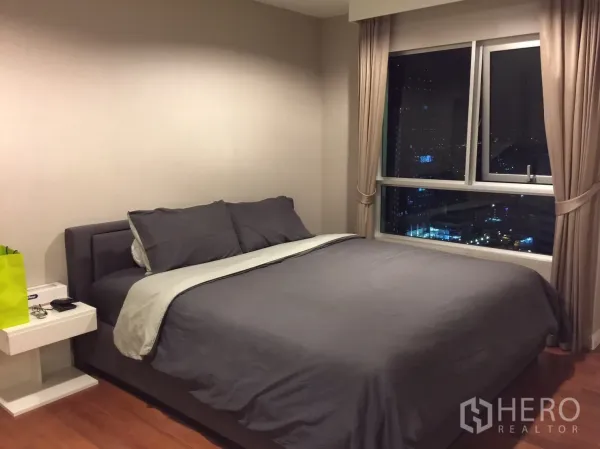 Condominium for rent in Huai Khwang, Bangkok - Master bedroom with king bed, wood floors and large window over Bangkok skyline.