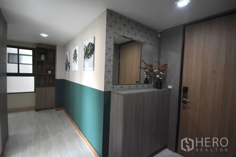 Condominium for rent in Khlong Toei, Bangkok - Entry hallway with built-in cabinet, decorative mirror, shelving and framed botanical prints in a modern condo.