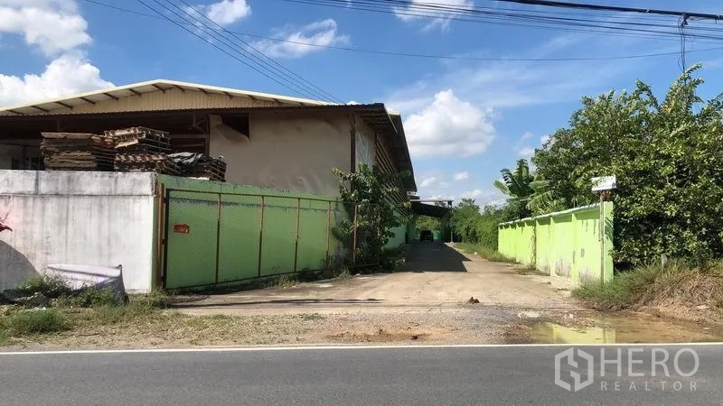 Factory for rent in Sam Khok, Pathum Thani - Street frontage view showing the gated driveway leading into the factory compound.
