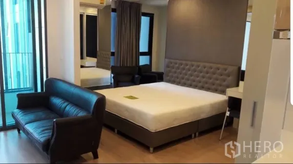 Condominium for rent in Bang Rak, Bangkok - Open-plan studio with bed, leather sofa and sliding door to a small balcony.