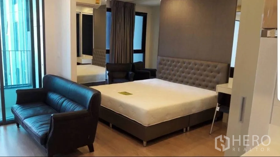 Condominium for rent in Bang Rak, Bangkok - Open-plan studio with bed, leather sofa and sliding door to a small balcony.