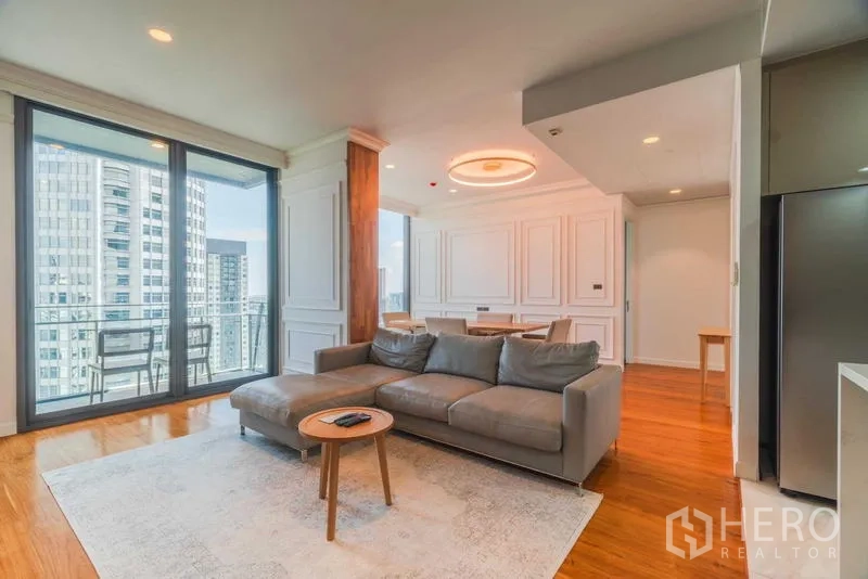 Condominium for rent or sale - Living room with L-shaped sofa, area rug, and access to balcony with skyline views.