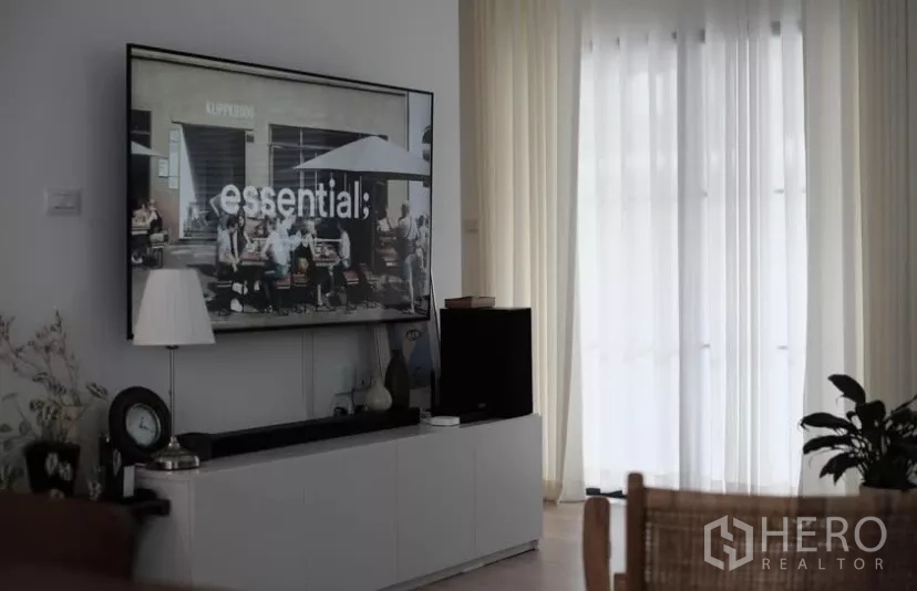 Townhouse for rent in Bang Phli, Samut Prakan - Media wall with large TV above a sleek cabinet facing full‑height curtains and balcony doors.