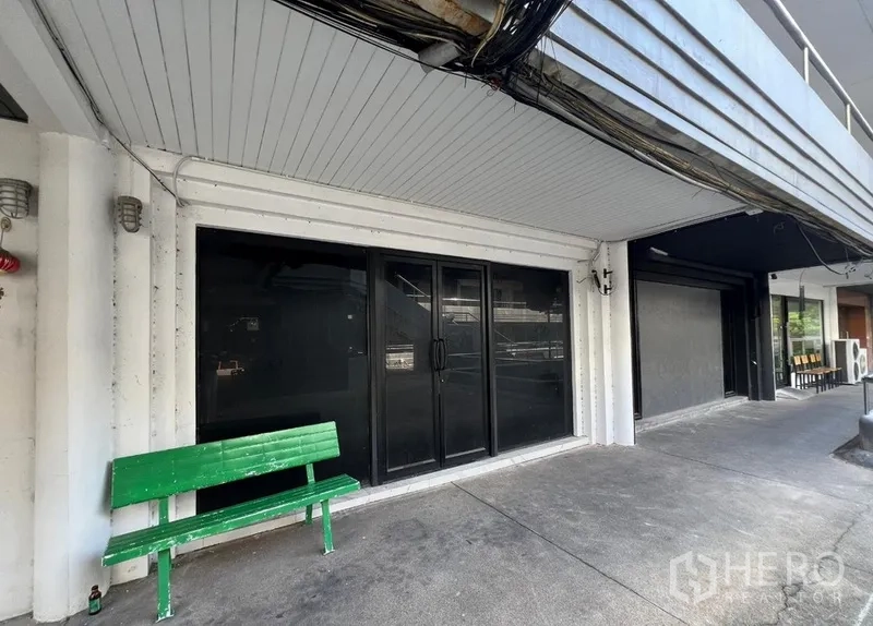 店屋 出租在Watthana, Bangkok - 骑楼外走道，整面黑色玻璃店面与绿色长椅。