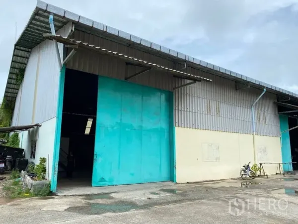 Warehouse for rent in Phra Samut Chedi, Samut Prakan - Warehouse exterior with teal steel sliding door, metal cladding and loading driveway.