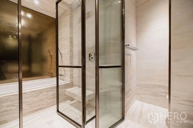 Condominium for rent - Glass-enclosed rain shower beside bathtub in marble-finished bathroom.