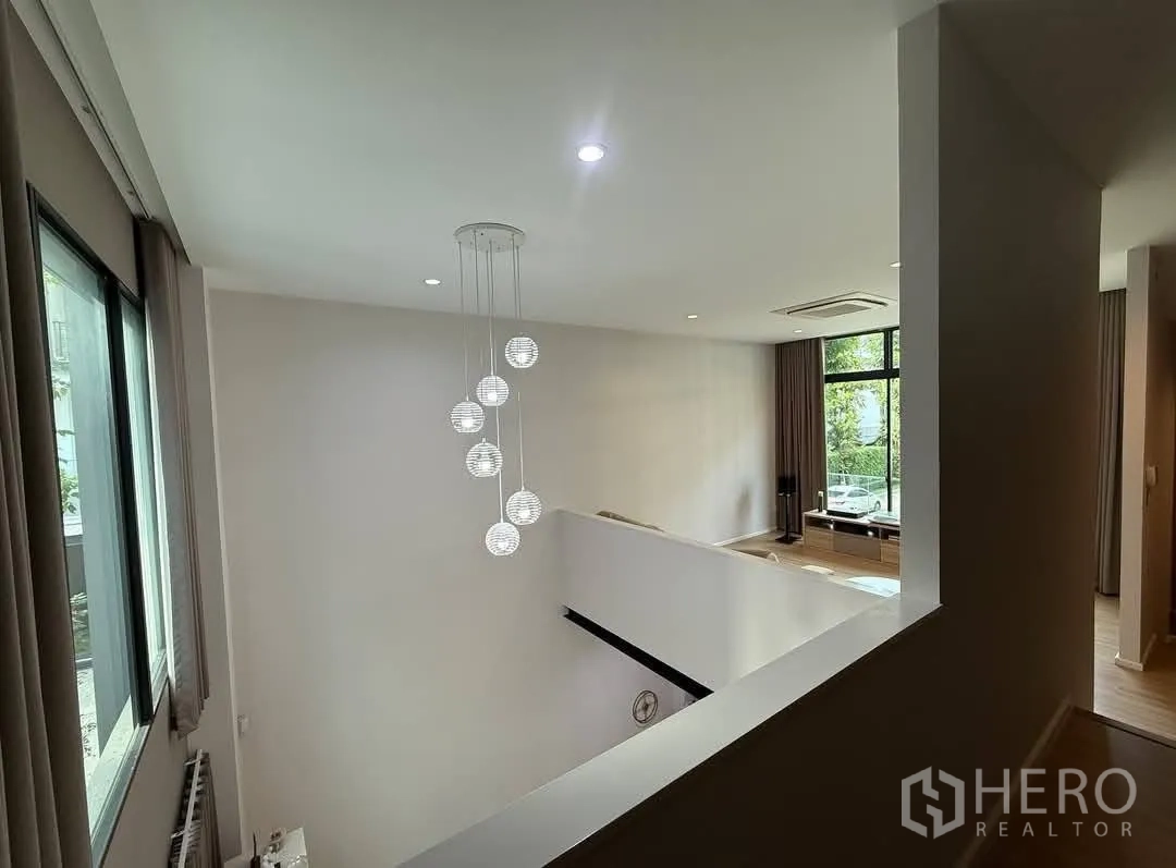 Townhouse for rent in Saphan Sung, Bangkok - View from mezzanine showing pendant lights and high-ceiling lounge with tall windows.