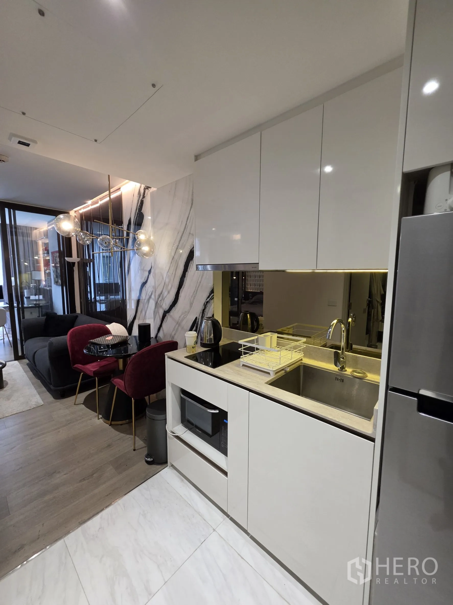 คอนโด for rent in Khlong Toei, Bangkok - ครัวสีขาวกะทัดรัดพร้อมอ่างล้างมือ เตา ไมโครเวฟ และตู้เย็น ติดกับห้องนั่งเล่นและมุมทานข้าว