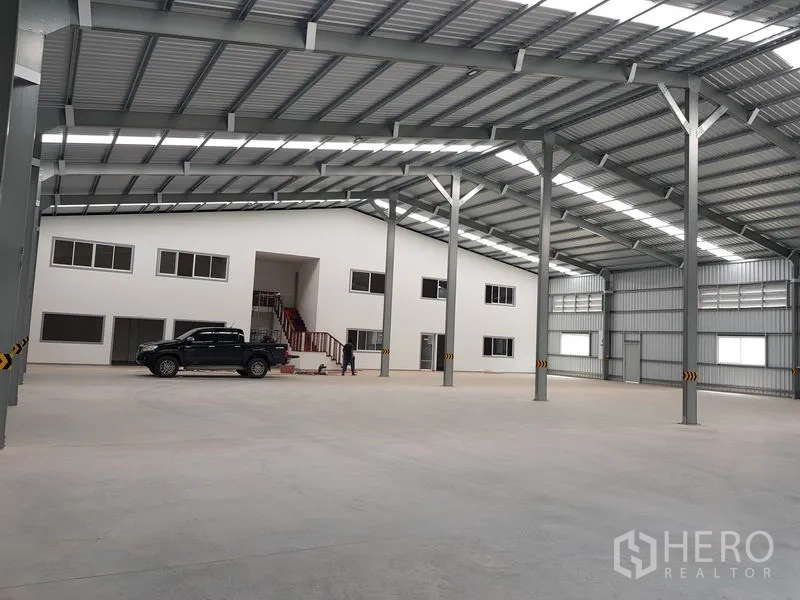 Warehouse for rent in Nonthaburi - Open-span warehouse hall with concrete floor and two-storey office block inside.