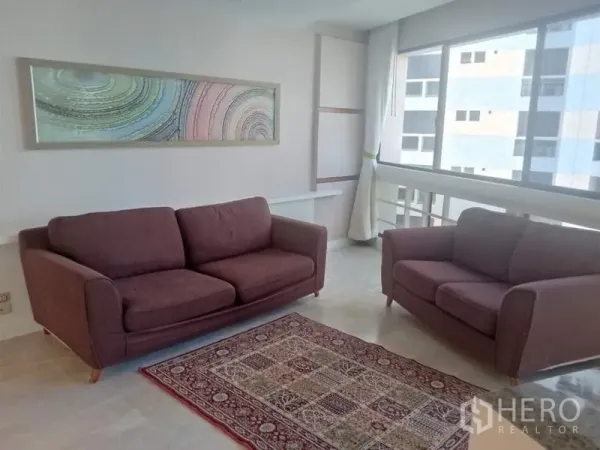 คอนโด ให้เช่าในKhlong Toei, Bangkok - ห้องนั่งเล่นสว่างด้วยโซฟาสีม่วงสองตัว หน้าต่างบานใหญ่ และงานศิลปะติดผนัง