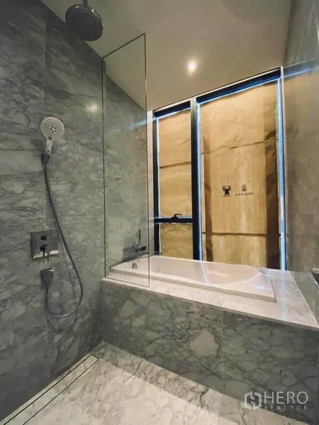Condominium for sale in Watthana, Bangkok - Bathroom with marble bathtub, glass rain shower, and tall window.