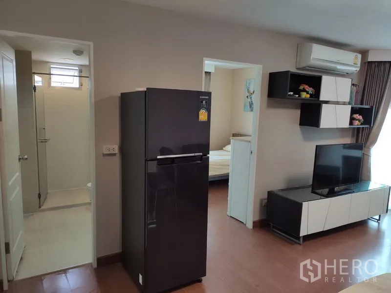 Condominium for rent in Huai Khwang, Bangkok - Living area showing TV wall, refrigerator and doorway to bathroom and second bedroom.