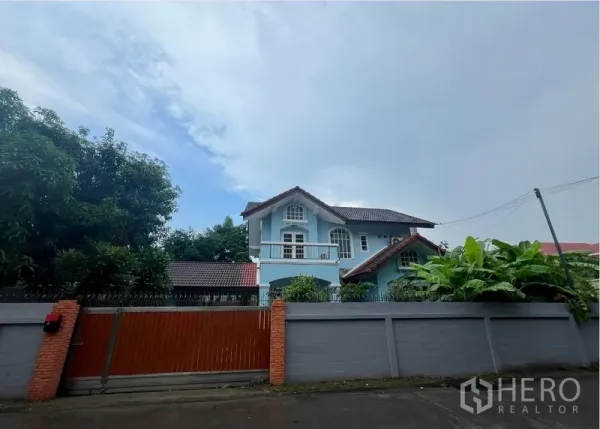 Detached House for rent in Bang Na, Bangkok - Two-storey blue detached house behind a high wall and wooden sliding gate on a quiet street