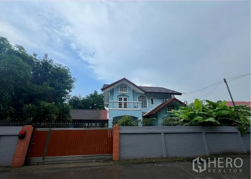 Detached House for rent in Bang Na, Bangkok - Two-storey blue detached house behind a high wall and wooden sliding gate on a quiet street