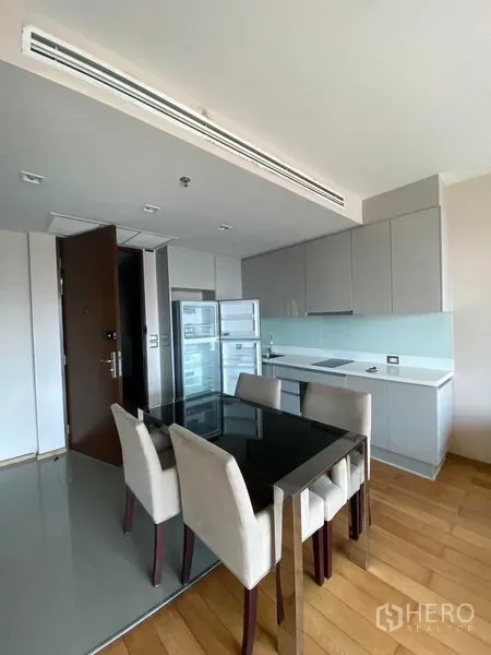 Condominium for sale in Ratchathewi, Bangkok - Open-plan kitchen with grey cabinets, glass backsplash, built-in hob, full-height fridge and a four-seat dining table.