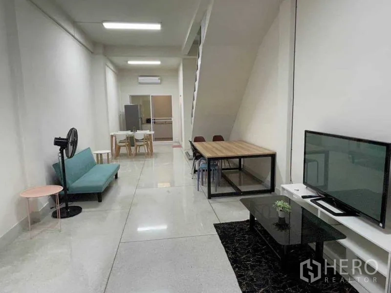Home Office for rent or sale in Watthana, Bangkok - Open-plan living space with sofa, TV console, dining table and staircase in a long room.