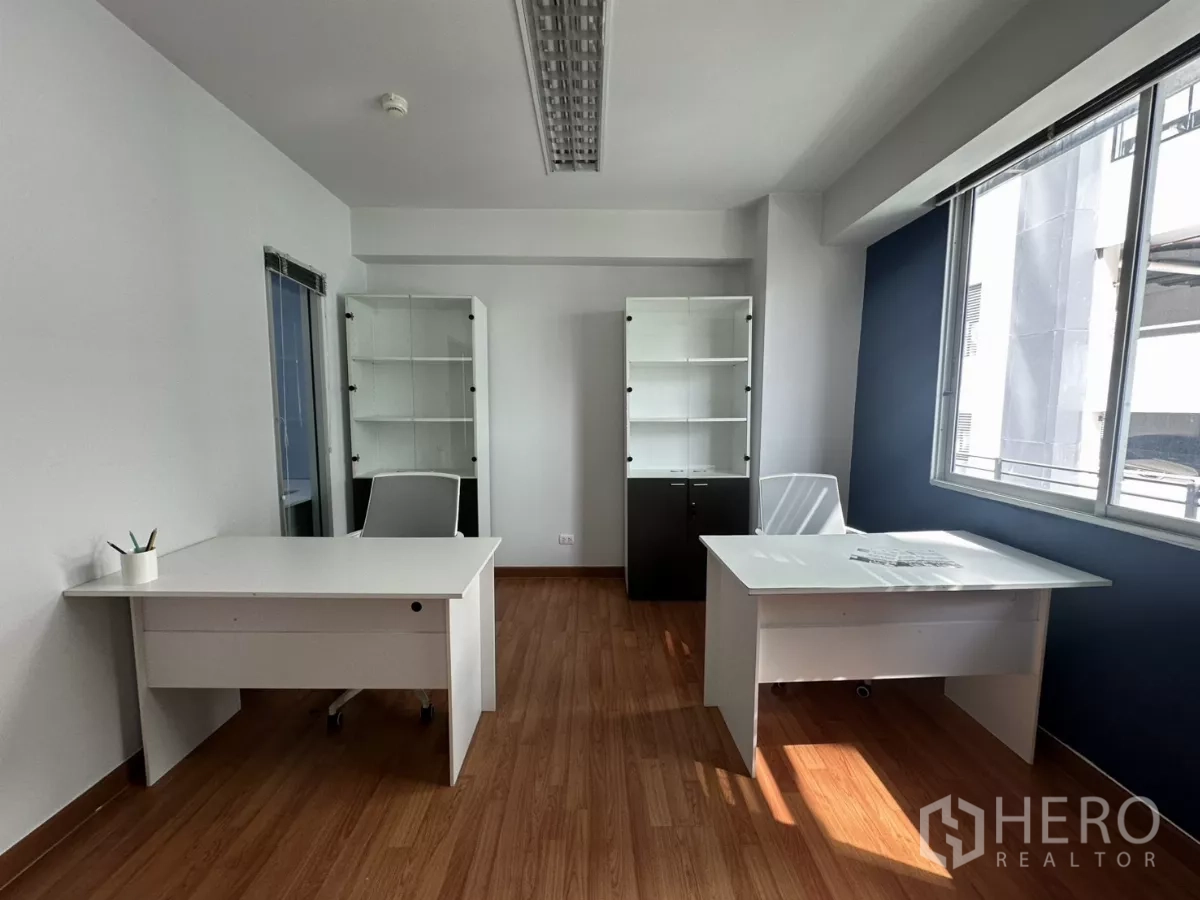 Office Space for rent in Watthana, Bangkok - Sunlit executive room with two desks, shelving cabinets and wood floors by a wide window.