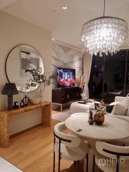 คอนโด ขาย - ห้องนั่งเล่น–รับประทานอาหารโทนอุ่น พร้อมโคมระย้า กระจกกลม พื้นไม้ และผนังกระจกติดระเบียง
