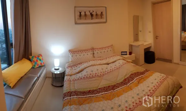 Condominium for rent in Khlong Toei, Bangkok - Cozy bedroom with double bed, window seat, bedside lamp, dressing table, and mirrored wardrobe.