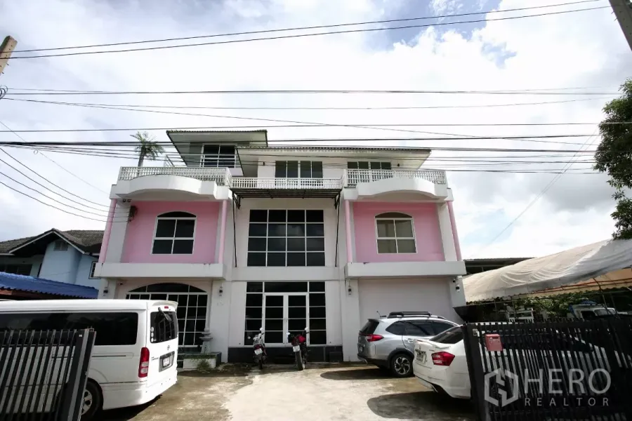 带办公室的家 出租在Prawet, Bangkok - 三层粉白外立面的住办楼，挑高玻璃门面与围合停车位。