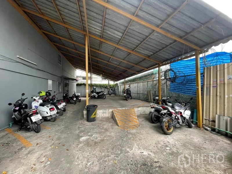 Apartment for sale in Mueang Samut Prakan, Samut Prakan - Covered motorbike parking under a metal roof beside the building.