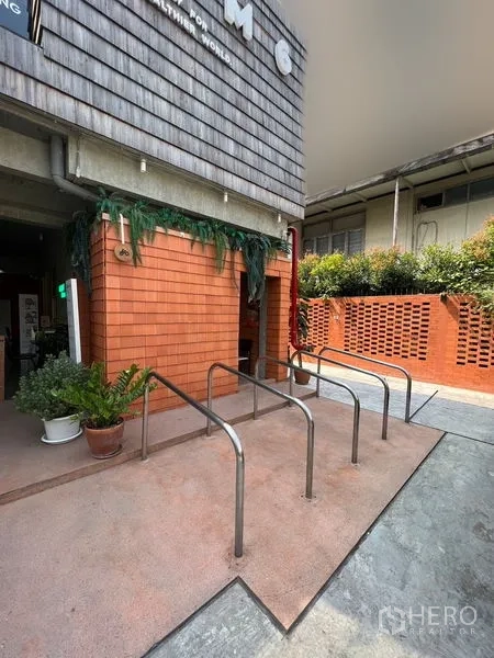 零售空间 出租在Watthana, Bangkok - 入口区设自行车架、橘色砖墙与绿植的零售物业。