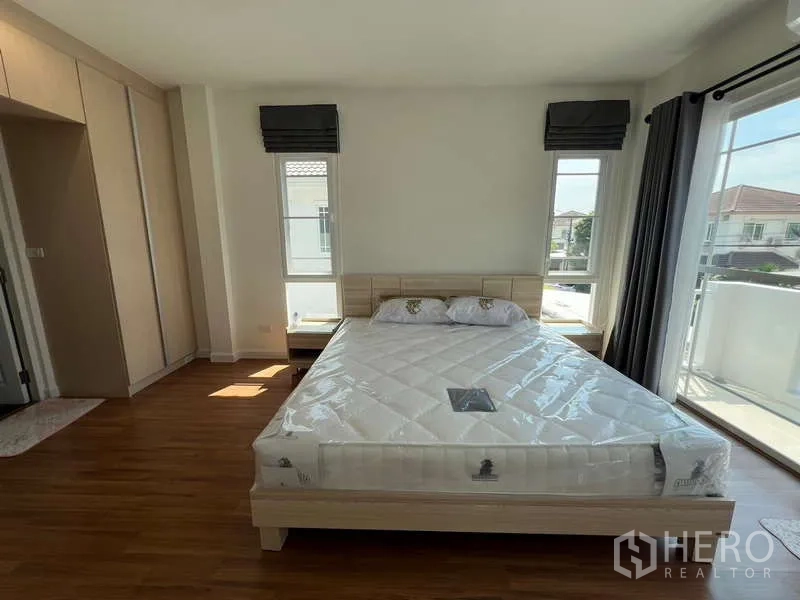 บ้าน ให้เช่าในBang Kapi, Bangkok - ห้องนอนใหญ่มีหน้าต่างบานกว้าง ประตูระเบียง และเตียงไม้โทนอ่อน