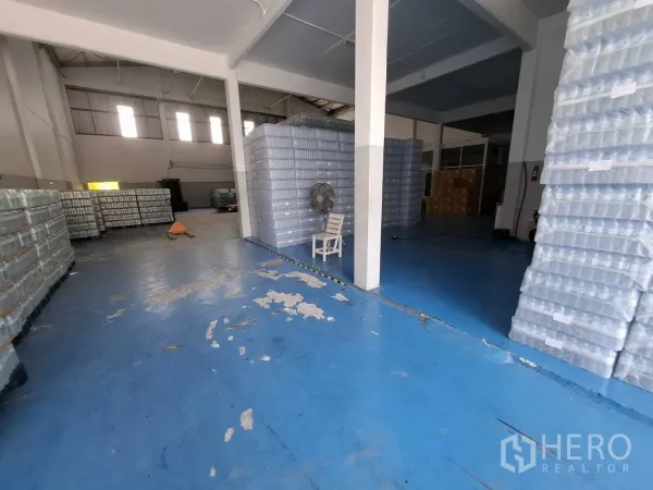 Factory for rent in Bang Phli, Samut Prakan - Open storage zone with support columns and palletized goods on a blue floor.