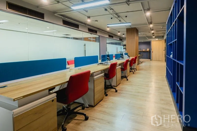 Office Space for rent - Row of workstations with red chairs, blue dividers and glass wall.