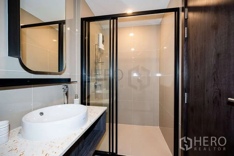 Condominium for rent or sale - Modern bathroom with glass-enclosed shower, vanity and dark wood door.
