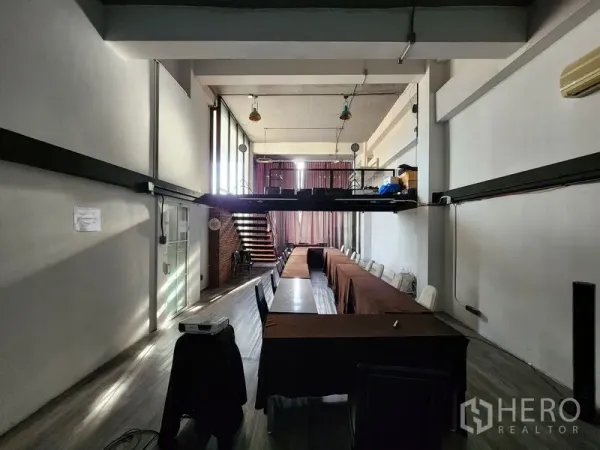 Home Office for rent in Mueang Nonthaburi, Nonthaburi - High-ceiling workspace with long meeting tables and a mezzanine platform at the rear.