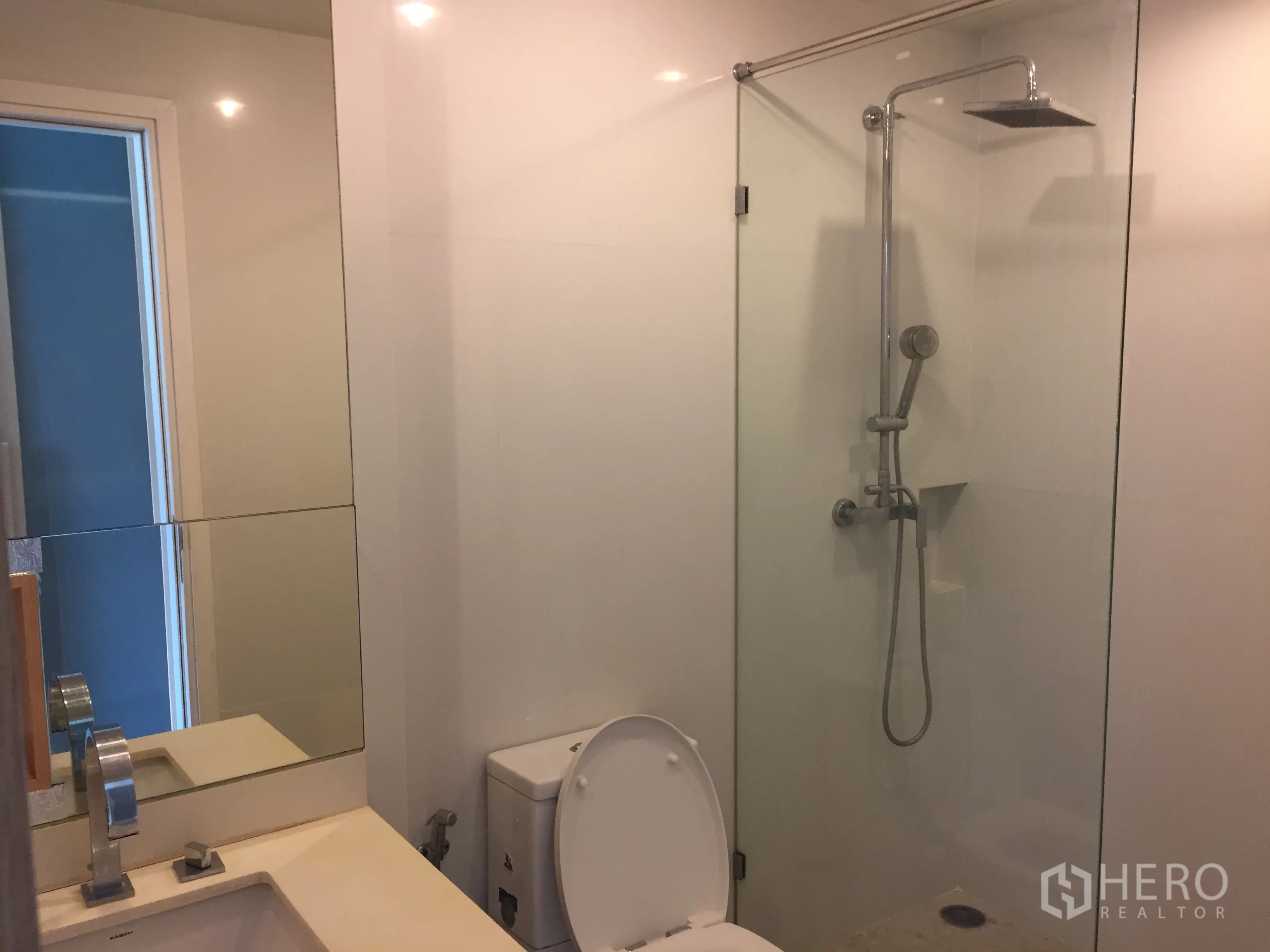 Condominium for sale in Watthana, Bangkok - Modern bathroom featuring a glass-enclosed rain shower, handheld shower, and white tiled walls.