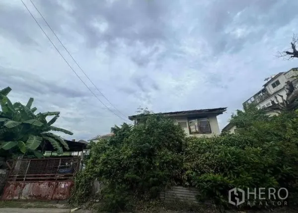 ที่ดิน ขายในPhra Khanong, Bangkok - ที่ดินมีพืชรกพร้อมบ้านสองชั้นเก่าและประตูเหล็ก ใต้ท้องฟ้ามีเมฆ