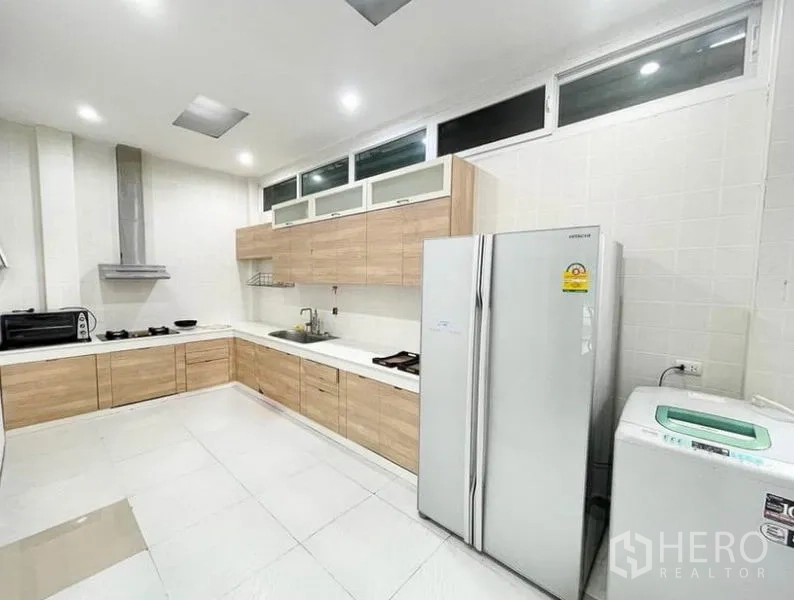 Townhouse for rent in Phasi Charoen, Bangkok - Modern L-shaped kitchen with wood cabinets, white countertops and a large refrigerator.