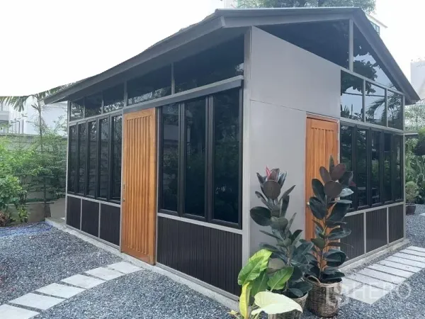 พื้นที่ขายปลีก ให้เช่าในSuan Luang, Bangkok - มุมมองอาคารกระจกสมัยใหม่ ประตูไม้ และกระถางต้นไม้ริมทางเดินกรวด