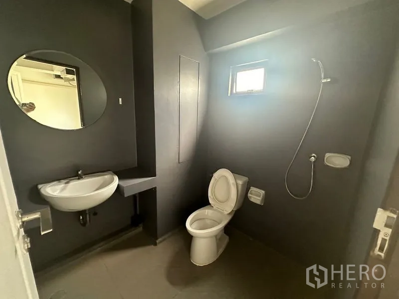 Home Office for rent in Phra Khanong, Bangkok - Dark-tone bathroom with round mirror, toilet and handheld shower.